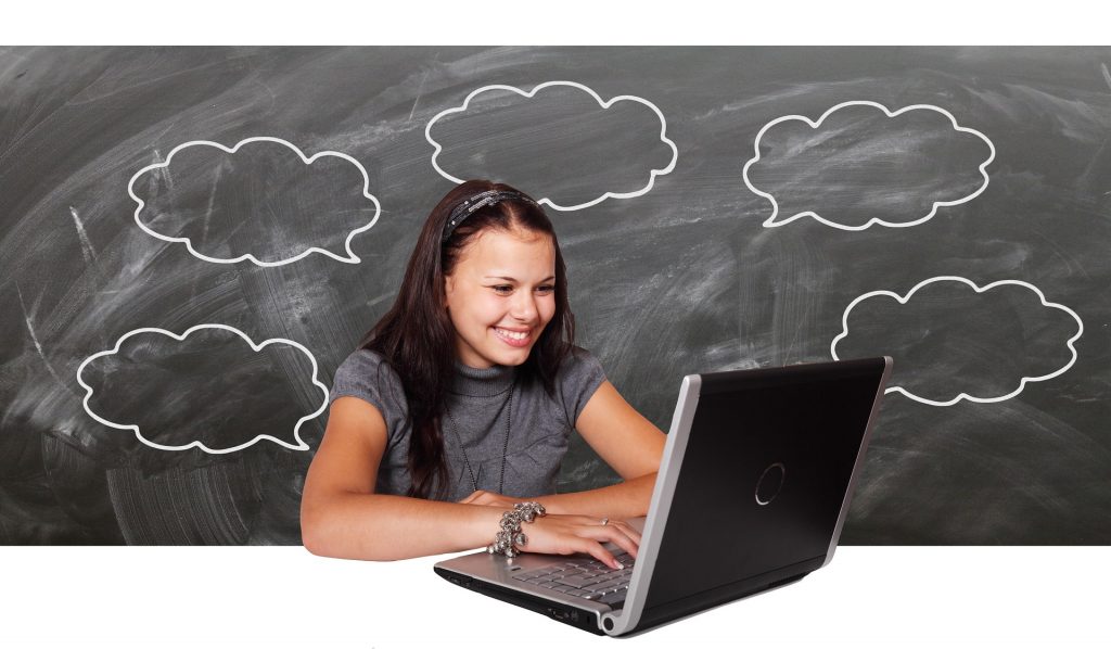 Eine junge Frau sitzt vor dem Laptop. Die junge Frau Freut sich. Im Hintergrund ist eine Tafel.