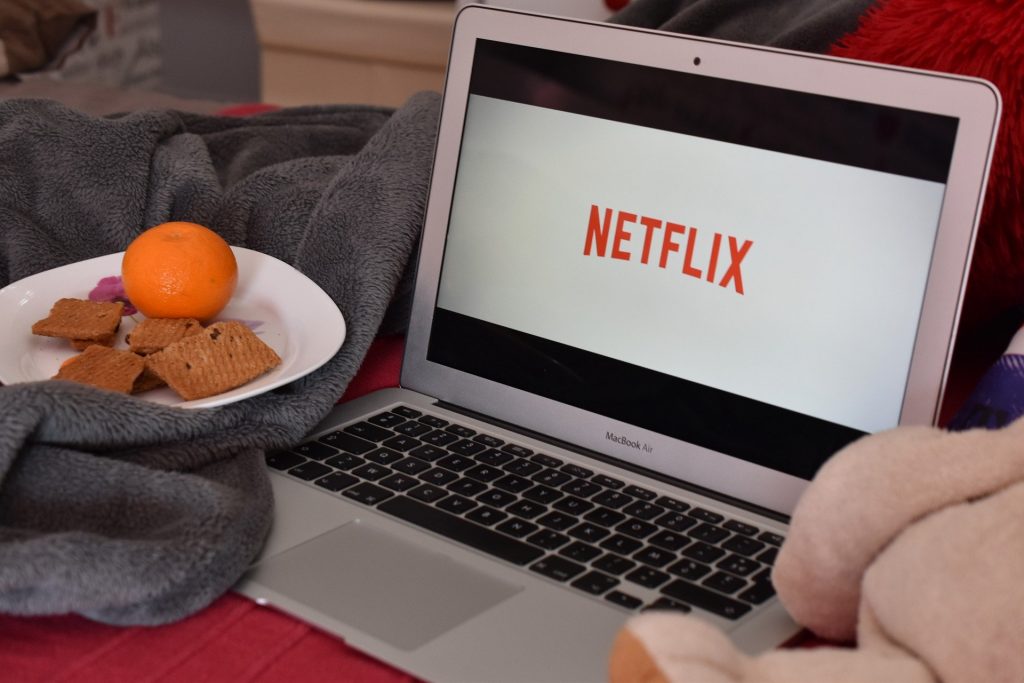 Ein Laptop steht neben einem Teller Obst und Keksen. Eingschaltet ist der Streamingdienst Netflix.