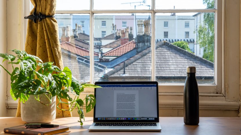 Ein Laptop steht zu Hause auf der Fensterbank. Man blickt dahinter über Häuserdächer.