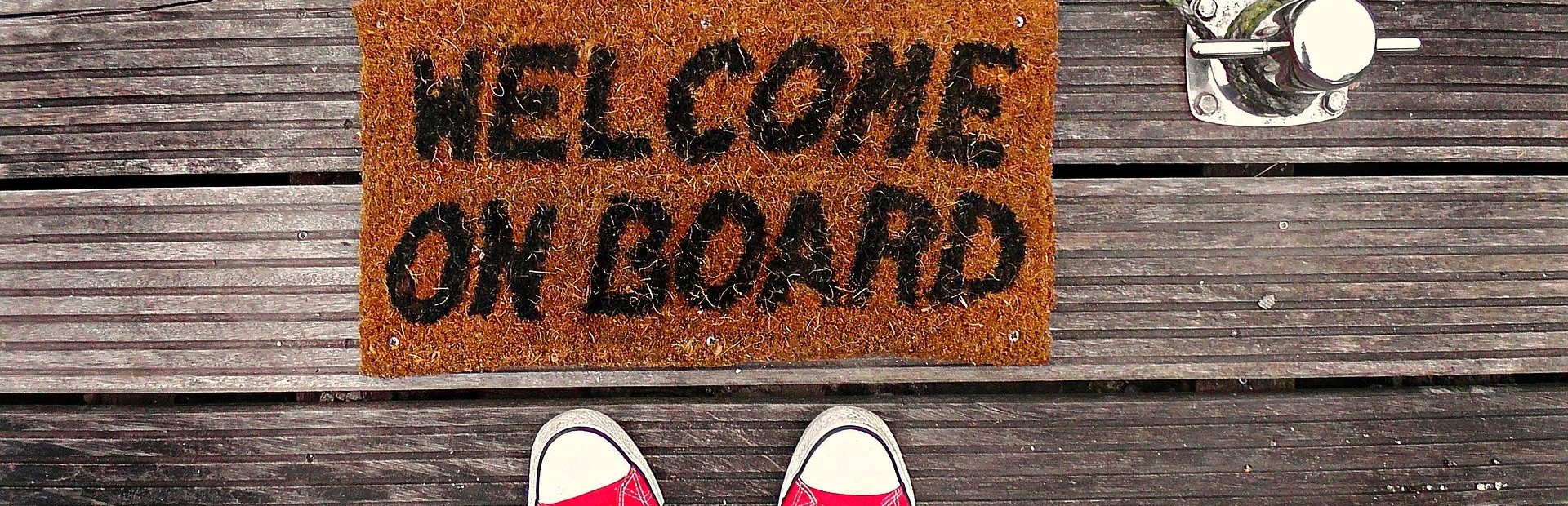 Digitales Onboarding: Ein Mensch steht vor einer Fußmatte mit der Aufschrift "Welcome on Board"