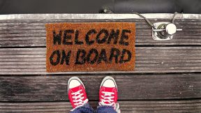 Digitales Onboarding: Ein Mensch steht vor einer Fußmatte mit der Aufschrift "Welcome on Board"