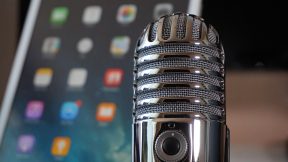 Ein Smartphone im Hintergrund und ein Mikrofon im Vordergrund soll einen Podcast symbolisieren, der digital aufgenommen wird und gehört wird.