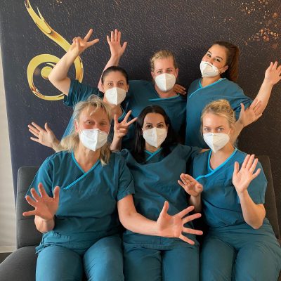 6 Frauen des Teams der Praxis Dr. Arnold posieren mit Mundschutz und grünen OP-Hemden.